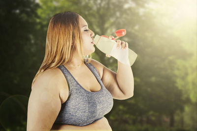 Side view of young woman drinking water at park