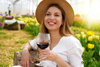 Relaxed beautiful woman enjoying a glass of red wine between tulips on spring time