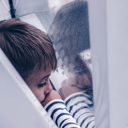 Thoughtful boy looking through wet window during monsoon