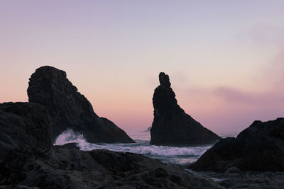 Rock formations on shore against sky during sunset