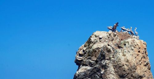 Low angle view of people on rock against clear blue sky