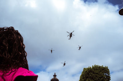 Low angle view of woman looking at helicopter flying against sky