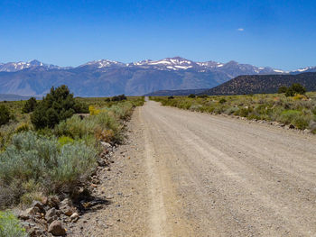 Dirt road by mountains against blue sky