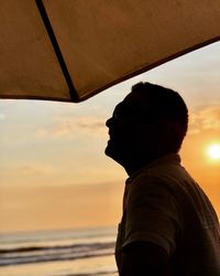 Portrait of man looking at sea against sky during sunset
