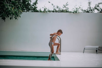 Side view of shirtless man standing by swimming pool against wall