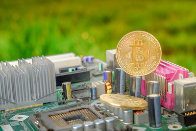 Close-up of bitcoins with motherboard against grassy field