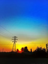 Silhouette electricity pylons on landscape against romantic sky at sunset