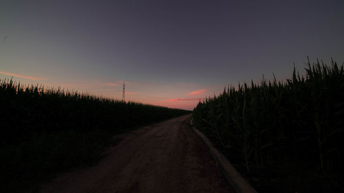 Road amidst field against clear sky at sunset