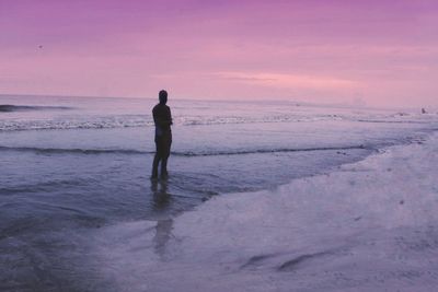 Silhouette man standing in shallow water at beach during sunset