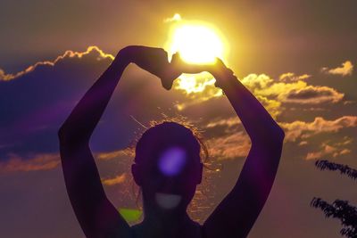 Silhouette woman with arms raised standing against sky during sunset