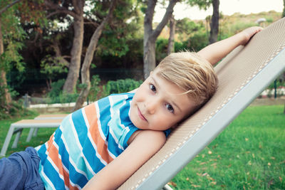 Portrait of cute boy lying on deck chair in park