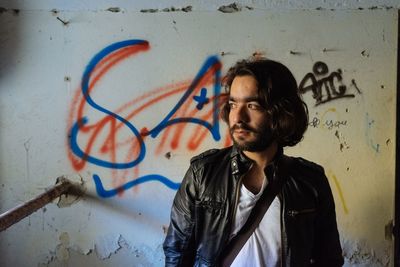 Thoughtful young man standing against graffiti wall