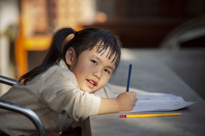 Portrait of girl drawing in book on table