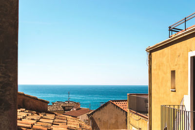 Buildings by sea against clear blue sky