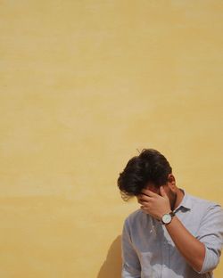 Young man obscuring face against yellow wall