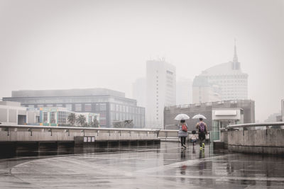 Rear view of family with umbrella walking on road during rain