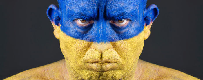 Close-up portrait of serious man with ukrainian flag body paint against black background