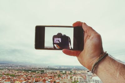 Cropped image of man holding mobile phone with camera image against sky