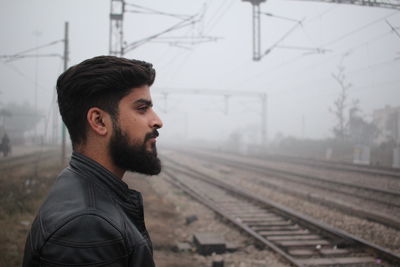 Side view of young man looking at railroad track