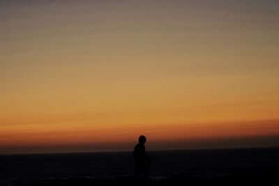 Silhouette man standing by sea against sky during sunset