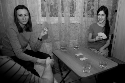 Smiling friends playing cards while sitting on table at home