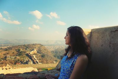 Side view of young woman standing on mountain against sky