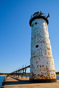 Lighthouse by sea against clear blue sky