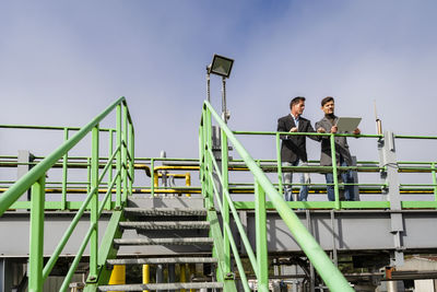 Mature businessman with colleague standing by railing at recycling center