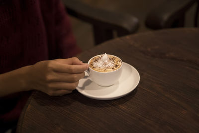 Close-up of hand holding coffee cup on table