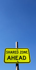 Low angle view of road sign against clear blue sky