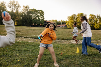 Happy girl splashing water while playing with friends on grass in playground at summer camp