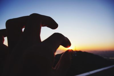 Close-up of hand holding sun during sunset