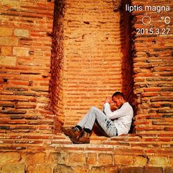 Young man sitting on brick wall