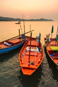 Sailboats moored on sea against sky during sunset