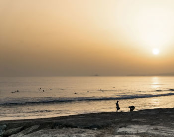 Silhouette people on beach against sky during sunset