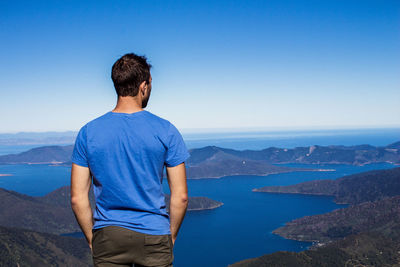 Rear view of man looking at mountains against blue sky