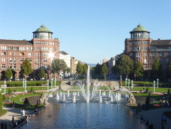 Fountain in lake against buildings in city