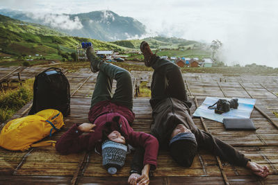 Man and woman lying on wood against mountains and sky