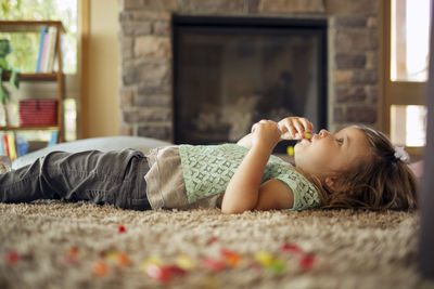 Girl eating food while lying on carpet at home