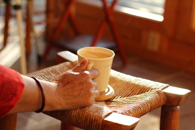 Cropped image of woman holding coffee cup over stool in cafe