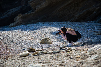 Beautiful woman crouching taking a picture of a pebbles beach at a creek side shot person