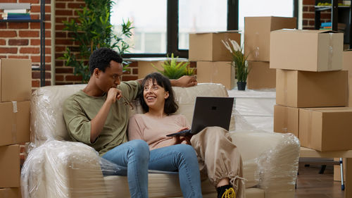 Happy woman with laptop sitting by man on sofa at home