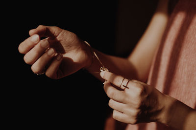 Midsection of woman wearing bracelet against black background