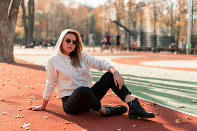 Portrait of young woman sitting at playing field during autumn