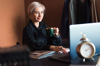 Fashion woman in black shirt working in modern work place or office with laptop and coffe cup