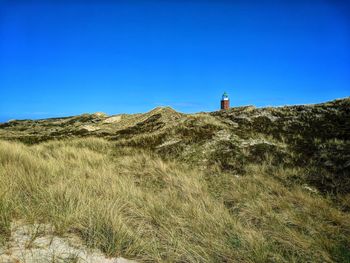 Lighthouse on field against clear blue sky