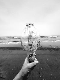 Person holding glass on beach against sky