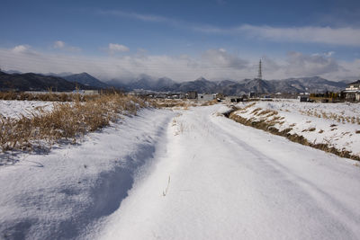 Snow covered road by field against sky