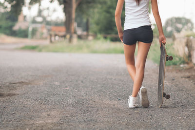 Rear view of woman with skateboard standing on footpath