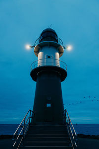 Lighthouse by sea against blue sky